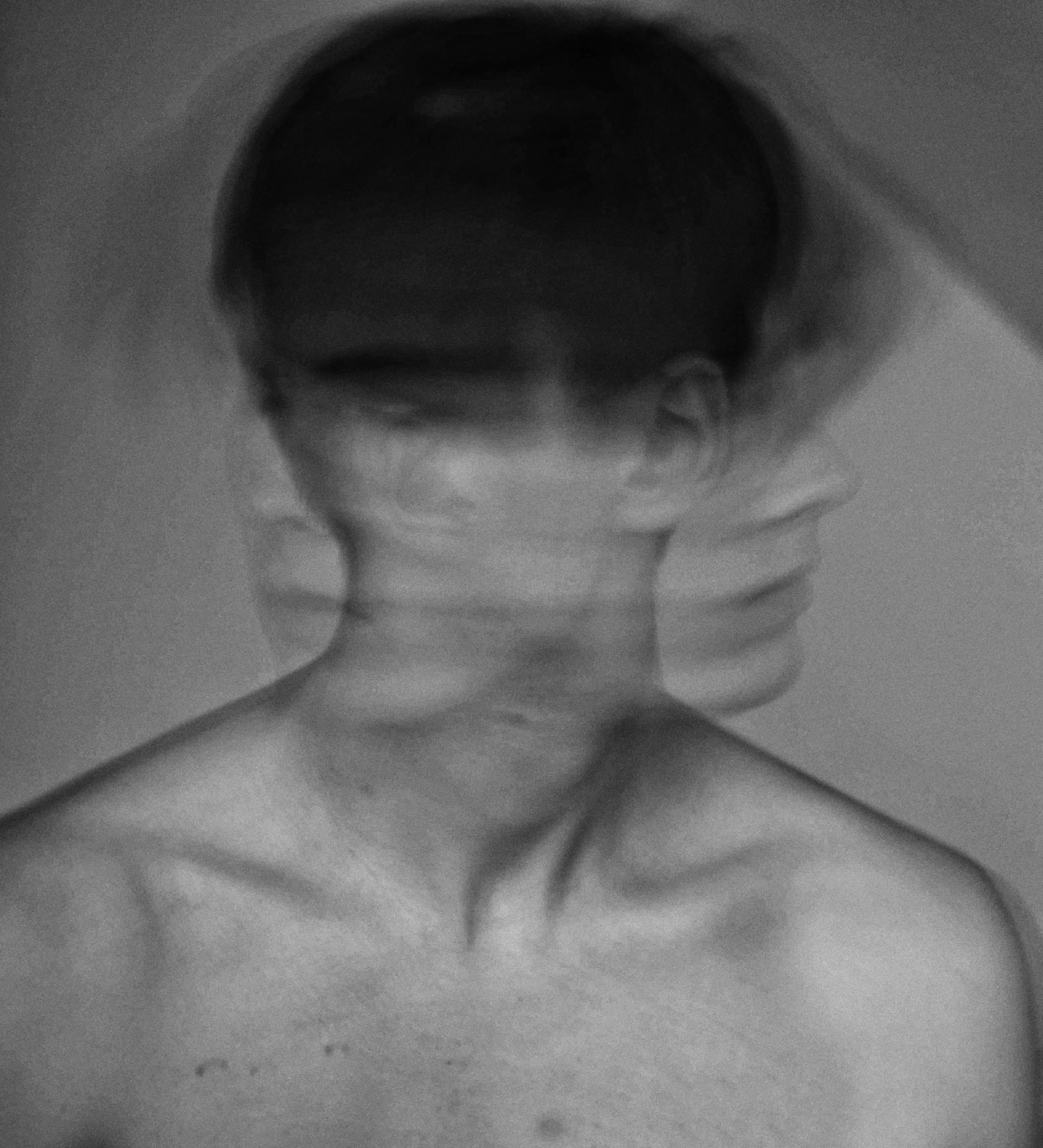 Bare shoulders and upper chest of a person in soft grayscale lighting with a subtle double exposure effect suggesting movement, set against a plain background with a calm and introspective mood